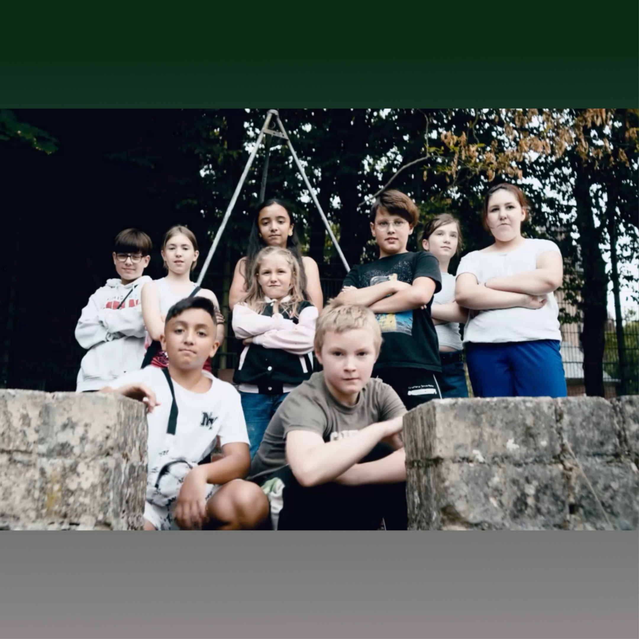 9 Kinder stehen, bzw. hocken hinter einer kleinen Mauer mit Öffnung und verschränken teilweise die Arme.