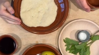 braune Teller mit Brotfladen, Äpfel, Salz und Bitterkräutern. Hände die den Teller halten und eine andere Hand, die den Becher mit Wein hält.