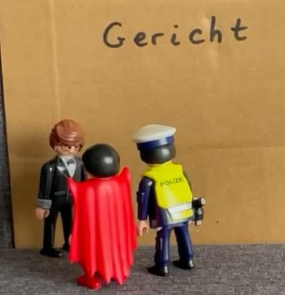 Pappe mit dem Wort 'Gericht' davor zwei Playmobilmännchen , die einen dritten befragen.